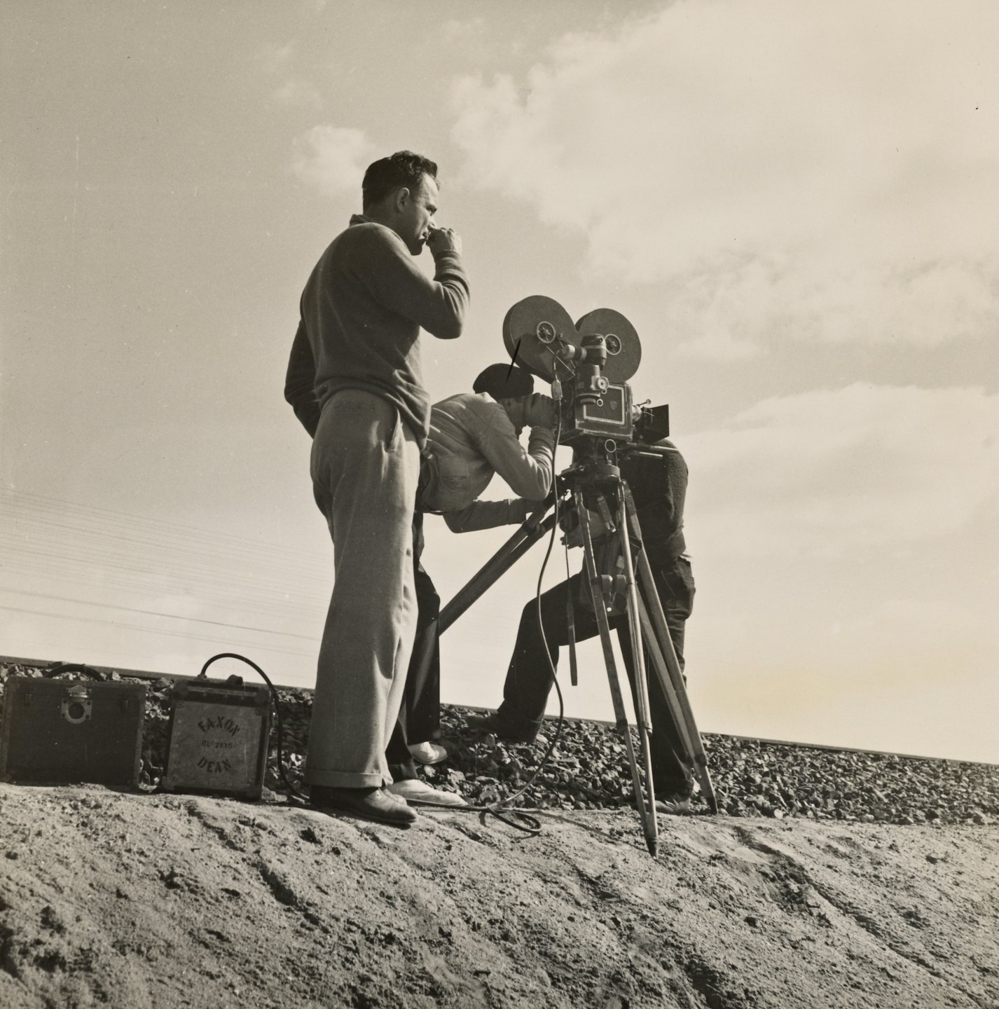 Men filming with vintage camera on sandy embankment.
