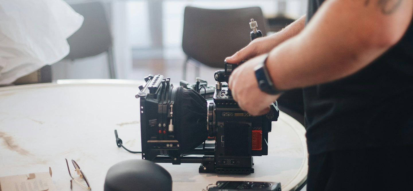Hands operating a cinema camera on a table.